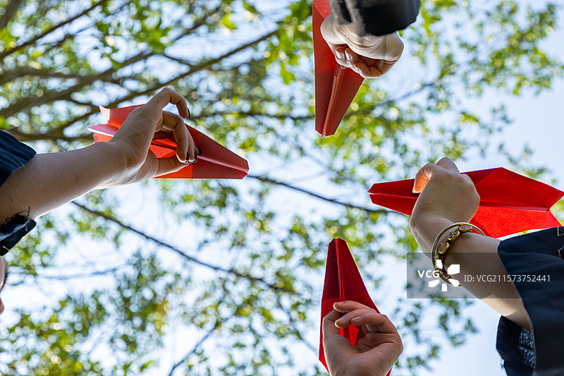 站在树下四个人穿着学士服拿着纸飞机举向天空图片素材