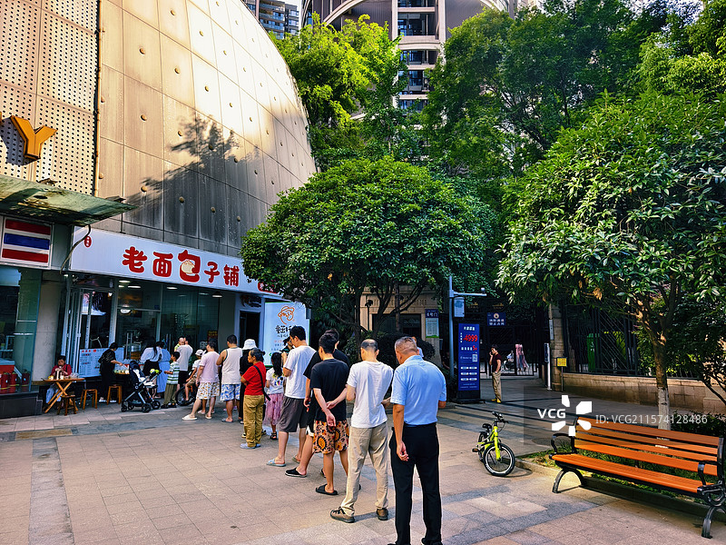 烟火人间早上的阳光洒在老面包子铺前，排队的人群和绿树成荫的街道构成了一幅温馨的画面。图片素材