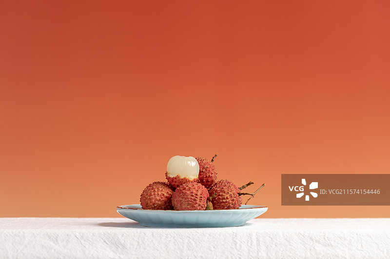 橙色背景下桌子上盘子里的荔枝特写镜头图片素材
