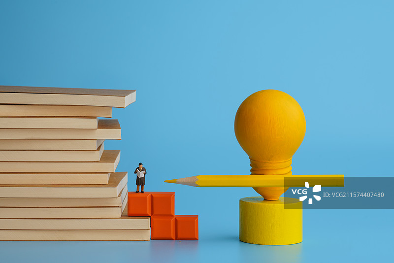 蓝色背景下堆叠书籍看书的男士和铅笔灯泡写镜头图片素材