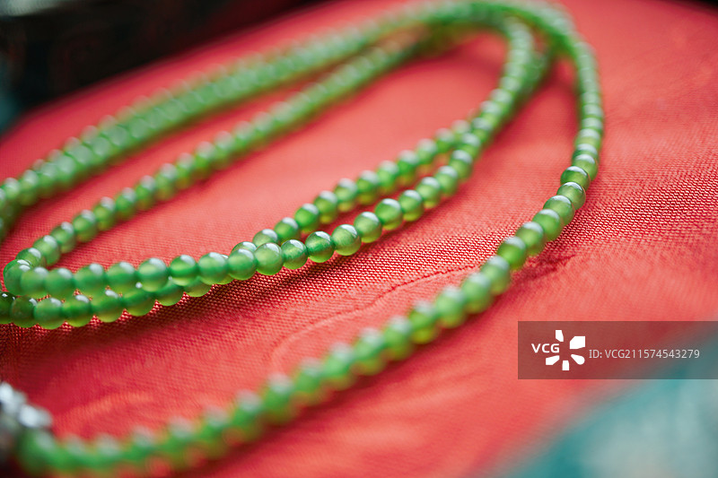 中国风和田玉碧玉翠绿玉珠串于锦缎红布之上图片素材