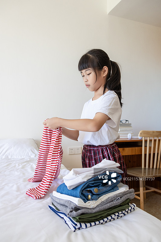 中国小女孩在卧室里叠衣服图片素材