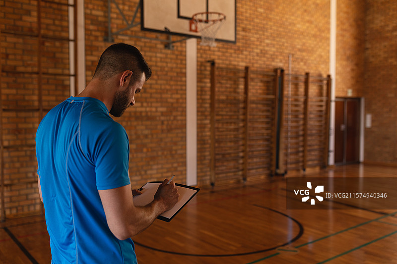 木制球场在顶灯下闪耀，展现出涂漆的地面线条、篮球架和墙壁杠。图片素材