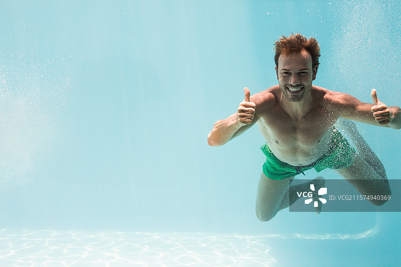 成年游泳者在水下漂浮，双手竖起大拇指，周围有气泡，穿着绿色泳裤。图片素材