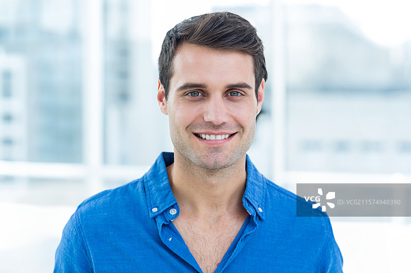 穿着蓝色衬衫的男子在办公室微笑，窗外是城市天际线的美景。图片素材