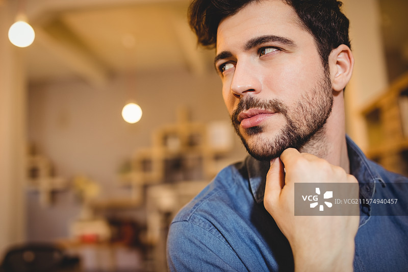 男子坐在咖啡馆的工作区桌子旁，周围有悬挂的灯泡和木制书架。图片素材