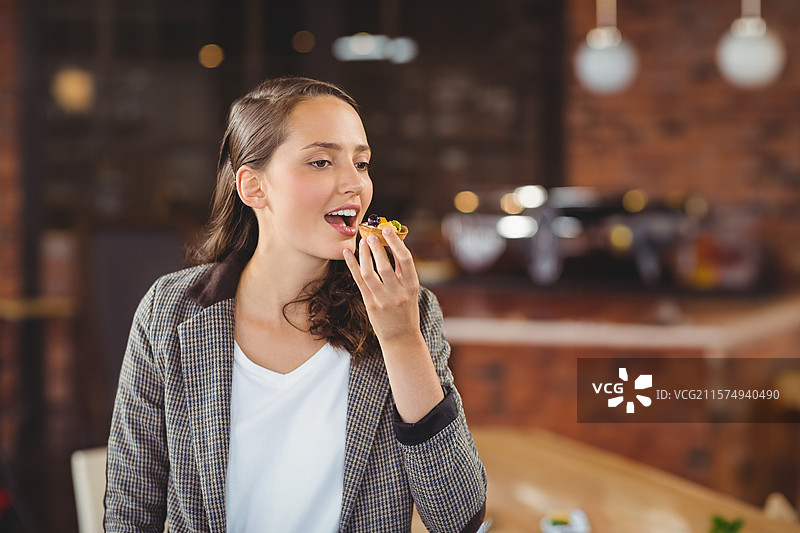 穿着格子西装的女性在砖墙和咖啡机旁的咖啡桌上拿着意式开胃小菜。图片素材