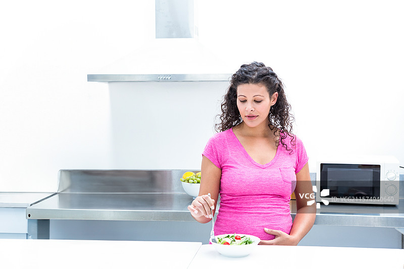 家用厨房的钢制台面上放着一个沙拉碗，旁边是一个盛有柠檬和苹果的水果碗。图片素材