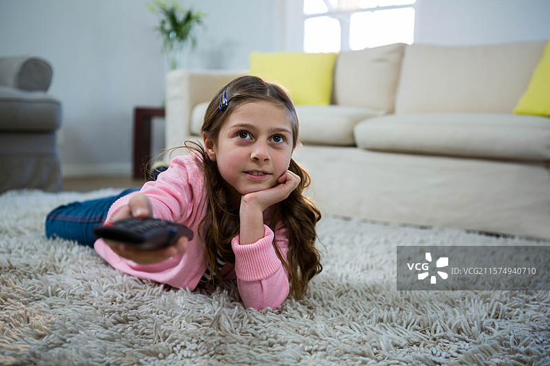 遥控器放在柔软的长毛地毯上，旁边是盆栽植物，靠近奶油色沙发和灰色扶手椅。图片素材