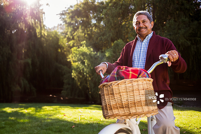 骑着白色自行车的男子，车篮里放着红绿格子毛毯，阳光透过树木洒下。图片素材