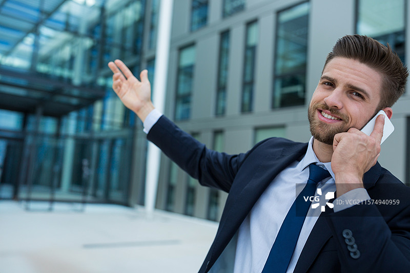 商人在企业广场使用智能手机并朝着玻璃钢结构的入口做手势图片素材