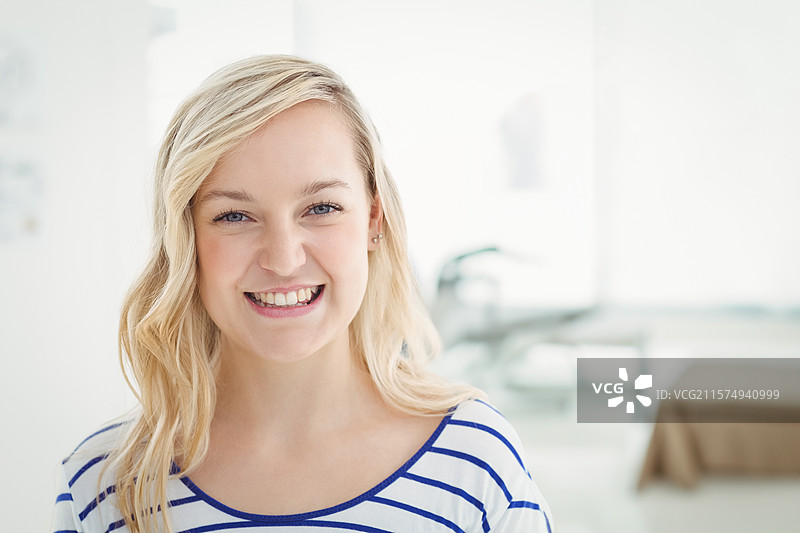 肤色白皙的女性穿着蓝条纹的白色上衣，在明亮的房间里微笑，背景装饰模糊。图片素材