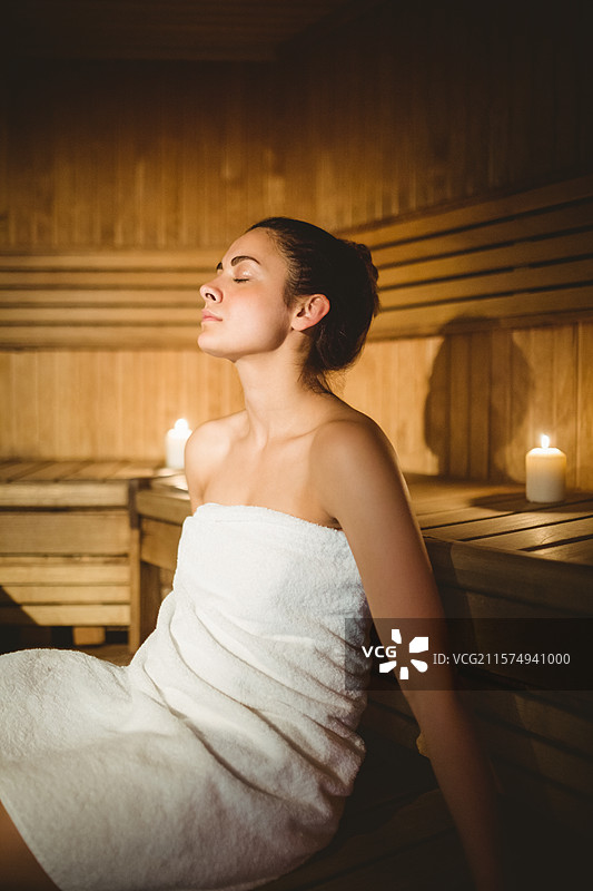 木质面板的桑拿小屋在蜡烛光下闪烁，木制长椅上放着白色毛巾，留有空白空间图片素材