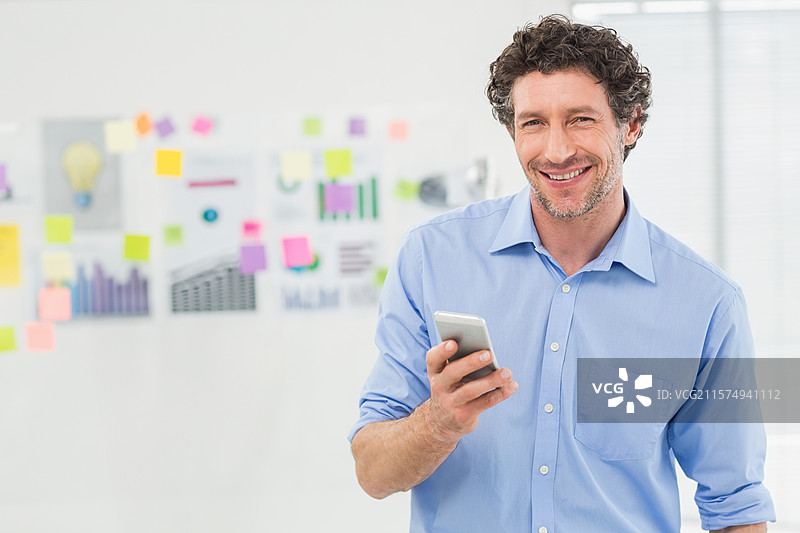 商人在办公室站着，手持智能手机，展示带有笔记和图表的白板。图片素材