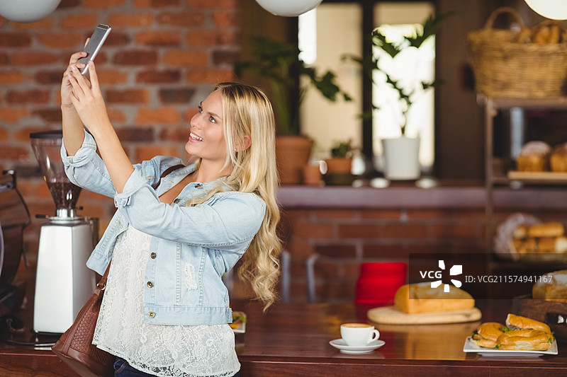 陶瓷咖啡杯冒着热气，旁边是木制台面上的面包卷，背景是咖啡店的砖墙。图片素材