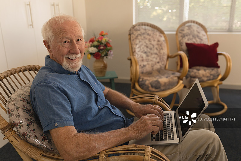 藤制扶手椅上放着笔记本电脑，窗帘旁边的青色边桌上展示着花卉。图片素材