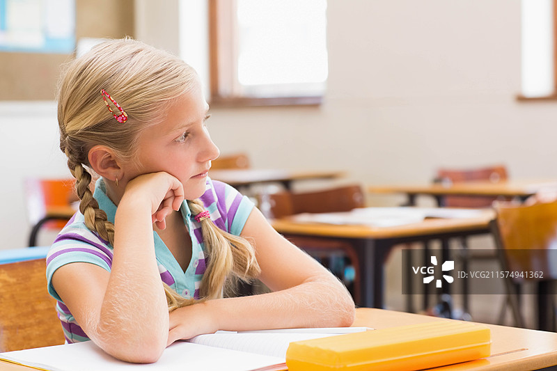 坐在学校课桌前的学龄女孩，凝视窗外，旁边有笔记本和文具盒，留白空间。图片素材