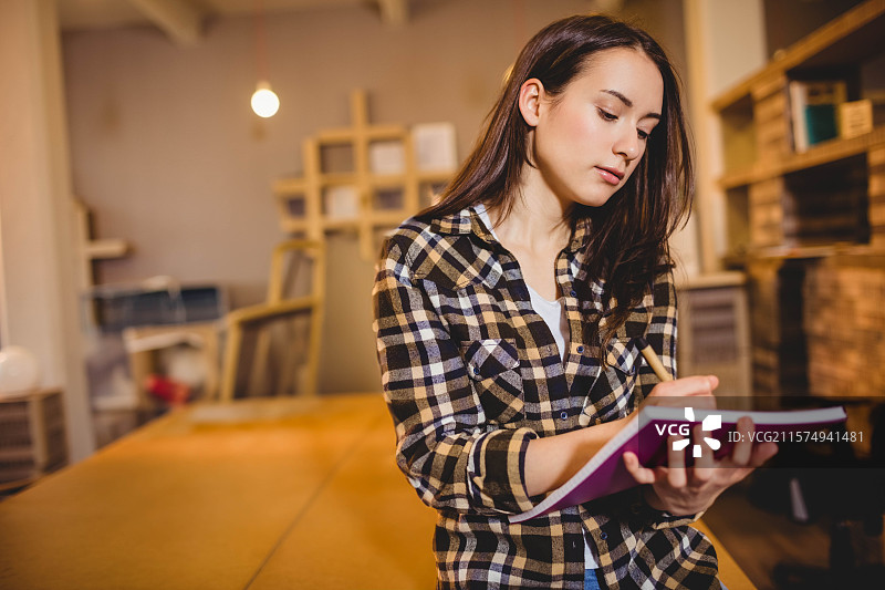 粉色笔记本静静地放在温暖灯光下的木桌上，旁边是装有盒子和相框的书架。图片素材