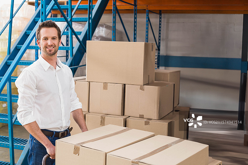 男子在仓库的混凝土地面上推着装满纸箱的手推车，留有空白空间图片素材