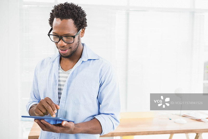 非裔美国男性站在办公室的窗帘旁，轻触蓝色平板电脑屏幕，留白空间图片素材
