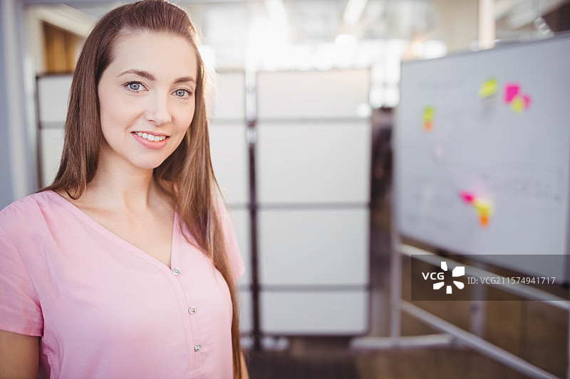 穿着粉色 blouse 的专业人士在开放式办公室中微笑，白板上贴满了便签，留有空白空间。图片素材