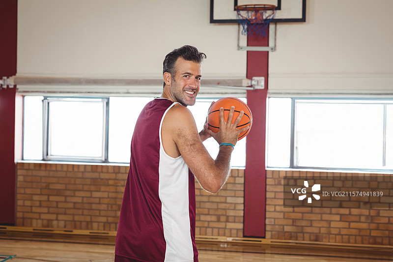 男篮球运动员穿着球衣，手持篮球在体育馆篮筐下准备投篮。图片素材