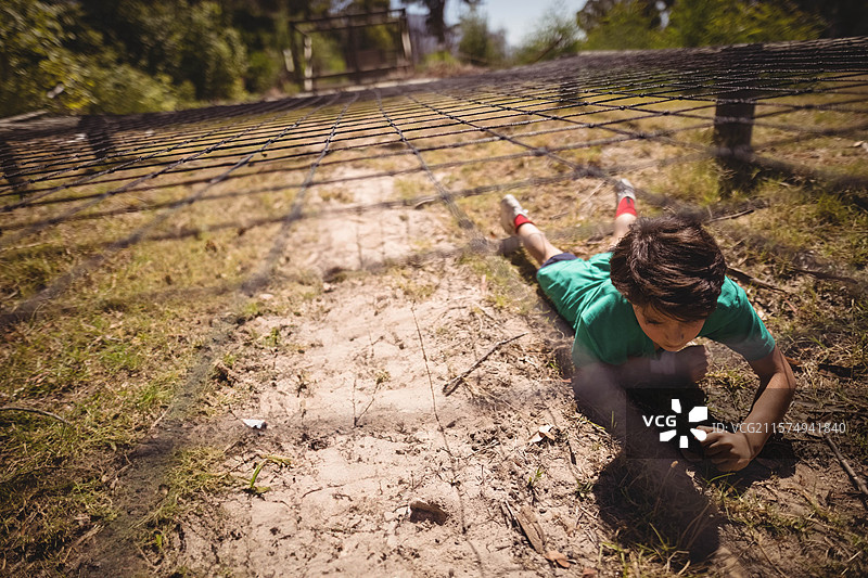 男孩在沙土小径上爬过尼龙障碍网，网格阴影投射在树林公园中。图片素材