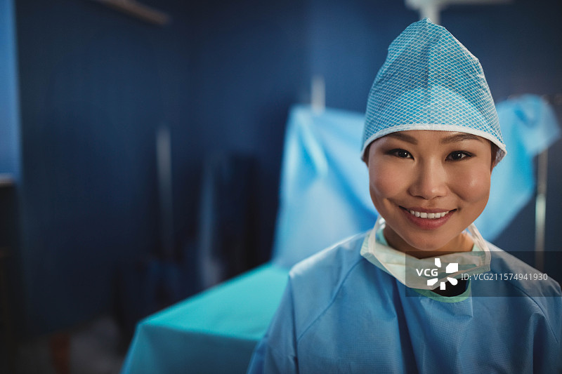 穿着手术帽的亚洲女性外科医生站在手术室的覆盖桌子右侧，留有空白空间。图片素材