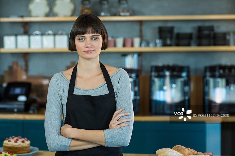穿着围裙的女性站在面包店的展示柜后，展示浆果蛋糕和面包。图片素材