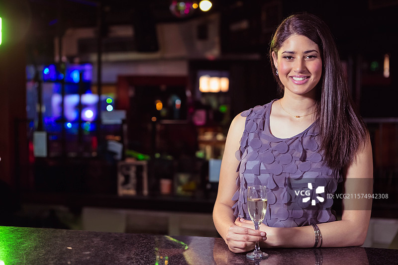二十多岁的女性在酒吧休息室的吧台后举着香槟杯，留有空白空间图片素材