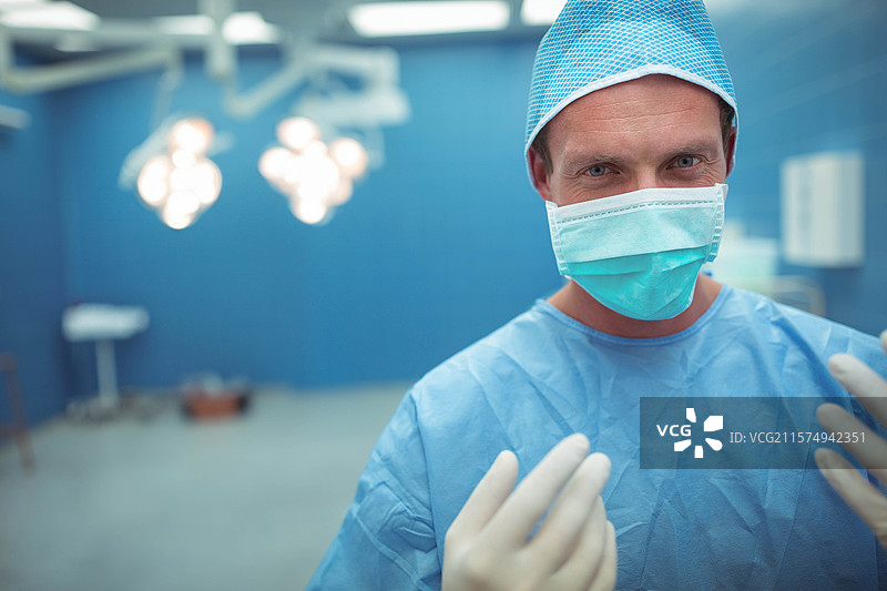 穿着手术服和口罩的男性外科医生站在手术室的手术灯下，留有空白空间图片素材