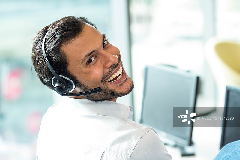 耳机静静地放在办公桌上，旁边是双显示器，阳光透过玻璃隔断洒入。图片素材