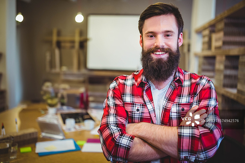 男子站在创意工作室里，使用笔记本电脑，周围散落着纸张、便利贴和咖啡杯。图片素材