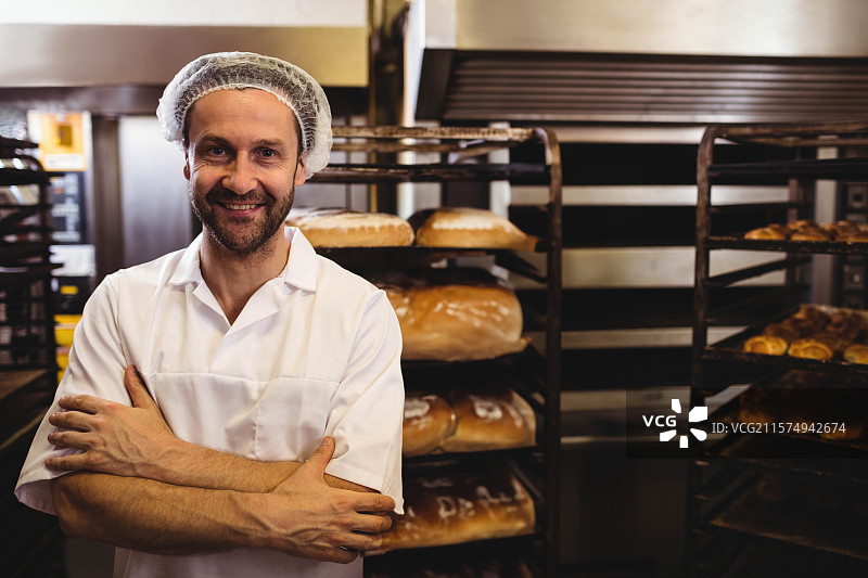 老年男性面包师在面包店的工业烤箱旁整理面包和糕点，旁边留有空白空间图片素材