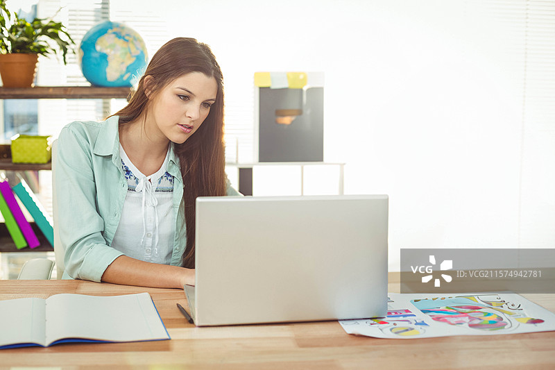 女性坐在桌子前，使用笔记本电脑和笔记本，在家庭办公室中工作，留有空白空间。图片素材