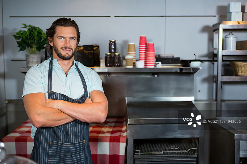 三十出头的男子站在咖啡馆柜台后，整理一次性杯子和玻璃罐。图片素材