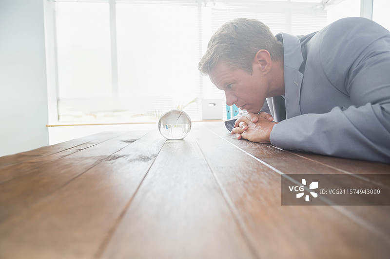 商务专业人士在办公室会议桌上向前倾身，观察窗帘旁的玻璃球。图片素材