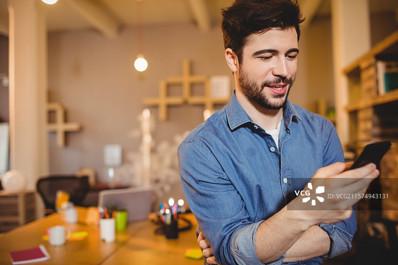 智能手机放在开放式办公室的桌子上，周围有笔记本电脑、咖啡杯和便利贴。图片素材