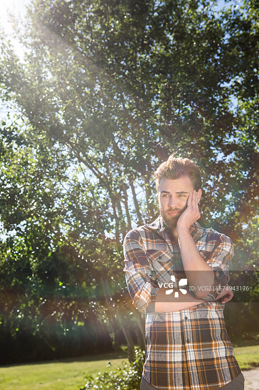 穿着格子衬衫的胡子男人在公园空地上交叉双臂，头部倾斜，镜头光晕，留白空间图片素材