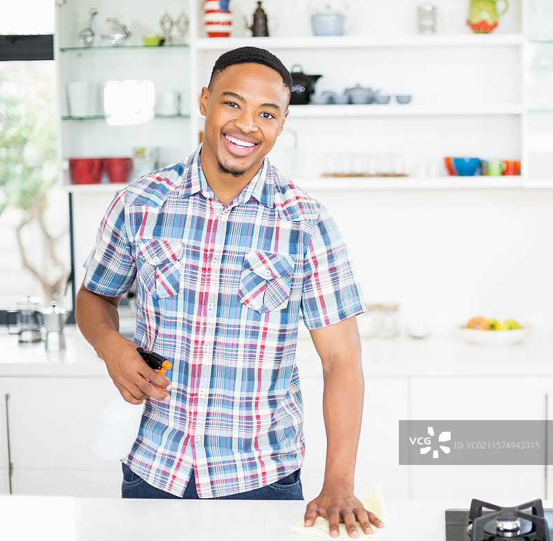 非裔美国男性在厨房岛上用喷雾瓶和布清洁台面图片素材