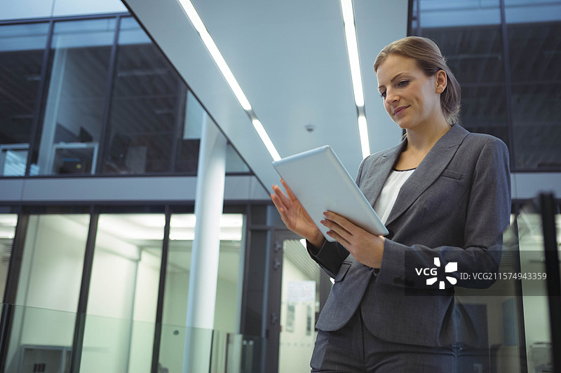 穿着西装的女商人在大堂的玻璃栏杆旁站着，手持白色平板，留有空白空间。图片素材