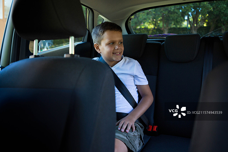 男孩坐在汽车座椅上，系着安全带，靠在头枕上，透过窗户看，留有空白空间。图片素材