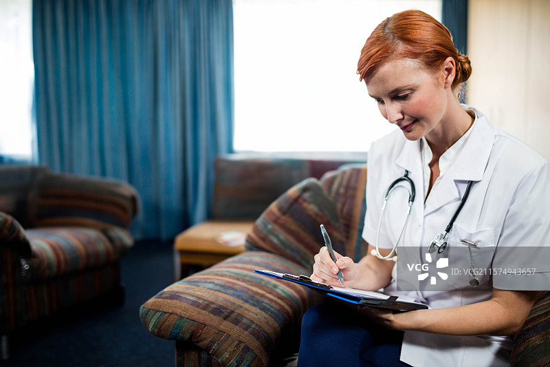 红发女性健康工作者穿着白色制服，在休息室里用夹板写字，留有空白空间图片素材