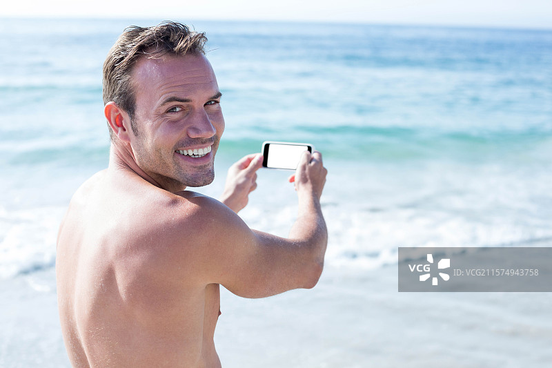 中年男子在沙滩水边微笑着，手持一部空白屏幕的智能手机图片素材