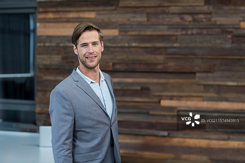 穿着灰色西装和蓝色衬衫的男子站在企业大堂，靠近玻璃隔断，留有空白空间图片素材