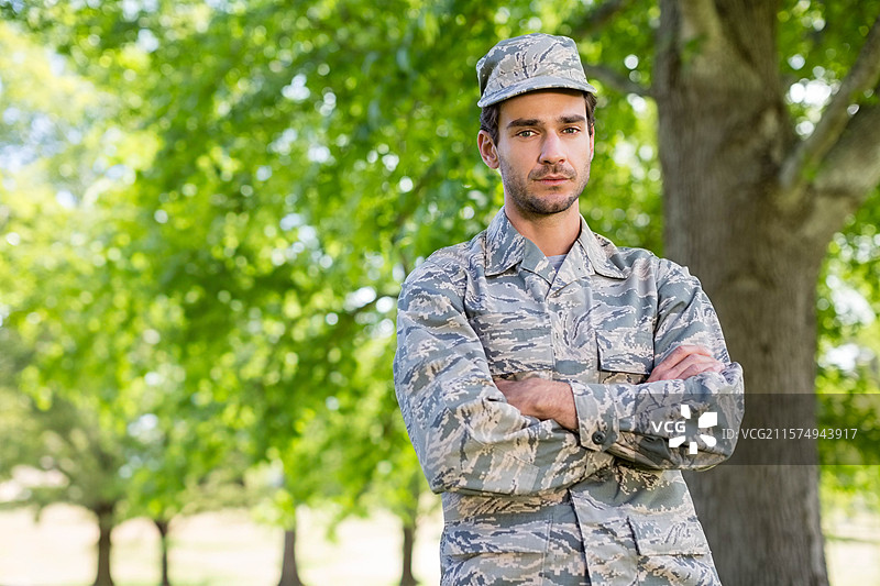 身穿迷彩夹克和巡逻帽的男性士兵站在林地中，留有空白空间图片素材