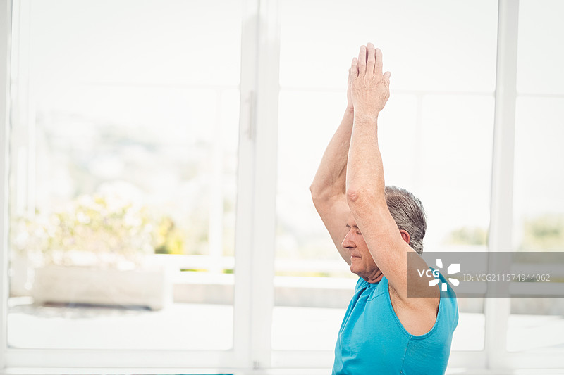 在高窗旁的瑜伽工作室里，一名男子正在做瑜伽拉伸，窗外有花盆。图片素材