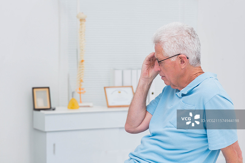 老年男子坐在咨询室里，戴着眼镜，柜子上有脊柱模型，留白空间图片素材