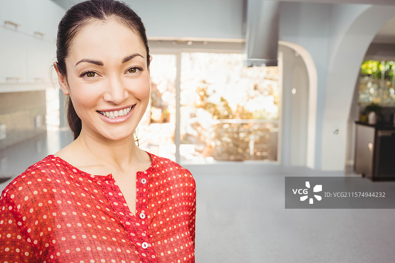 穿着红色上衣的女人在厨房里微笑，站在滑动玻璃门旁。图片素材
