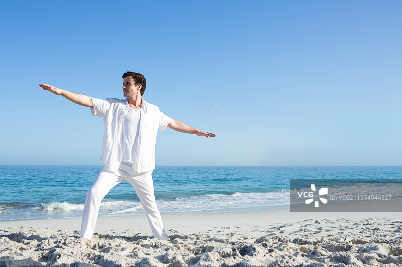 男子在海滩上练习瑜伽拉伸，身后是轻柔的海浪。图片素材